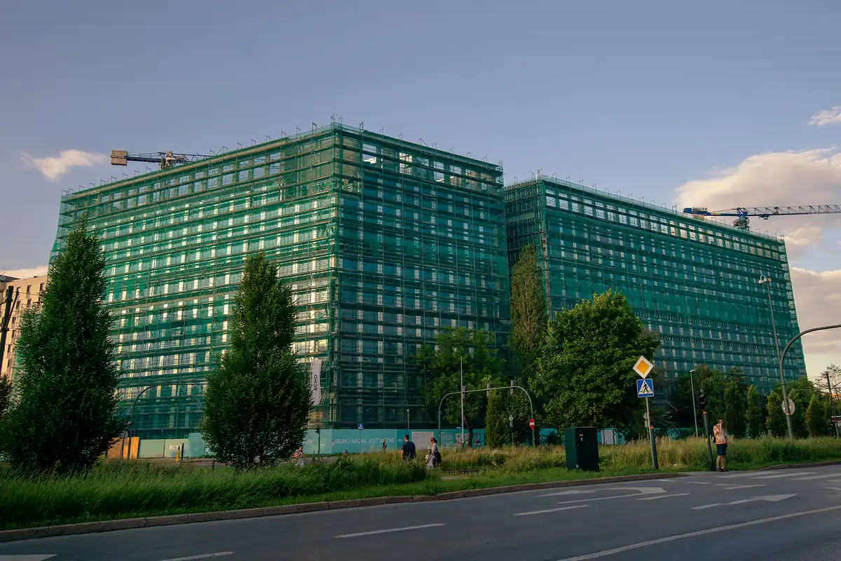 Rusztowanie elewacyjne obudowane zieloną siatką ochronną na całej wysokości budynku