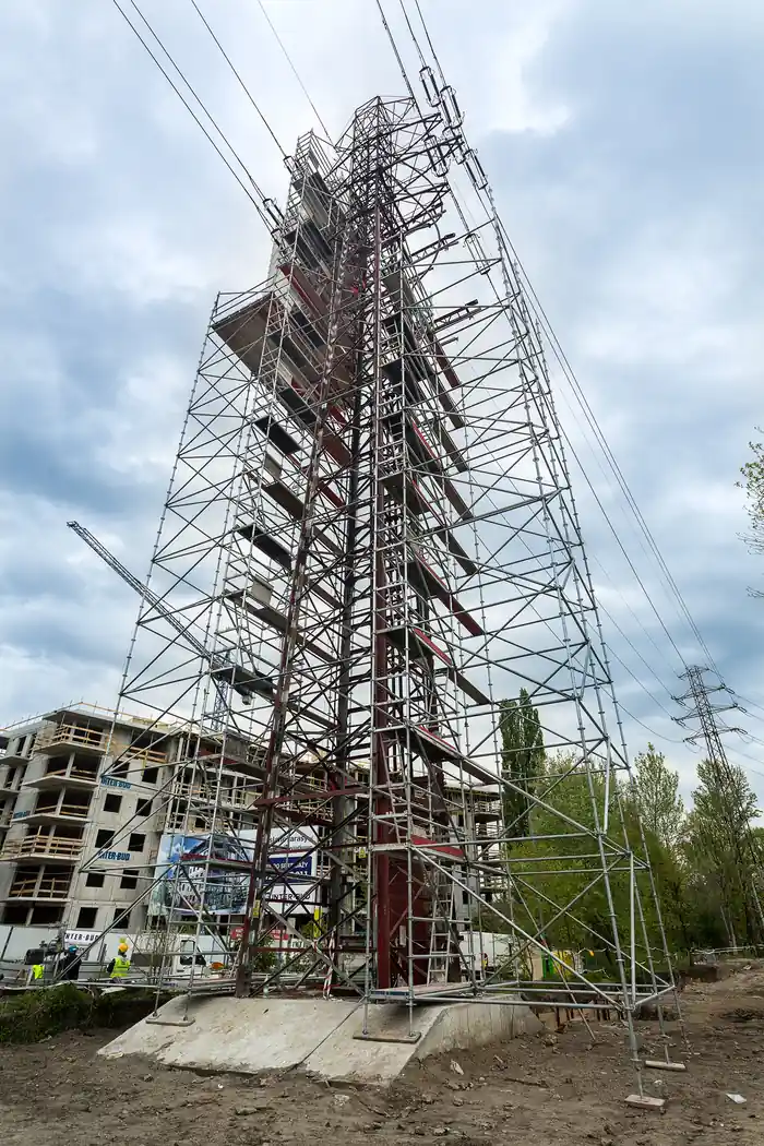Metalowe rusztowanie wieżowe ustawione na zewnątrz, w tle napowietrzne linie energetyczne